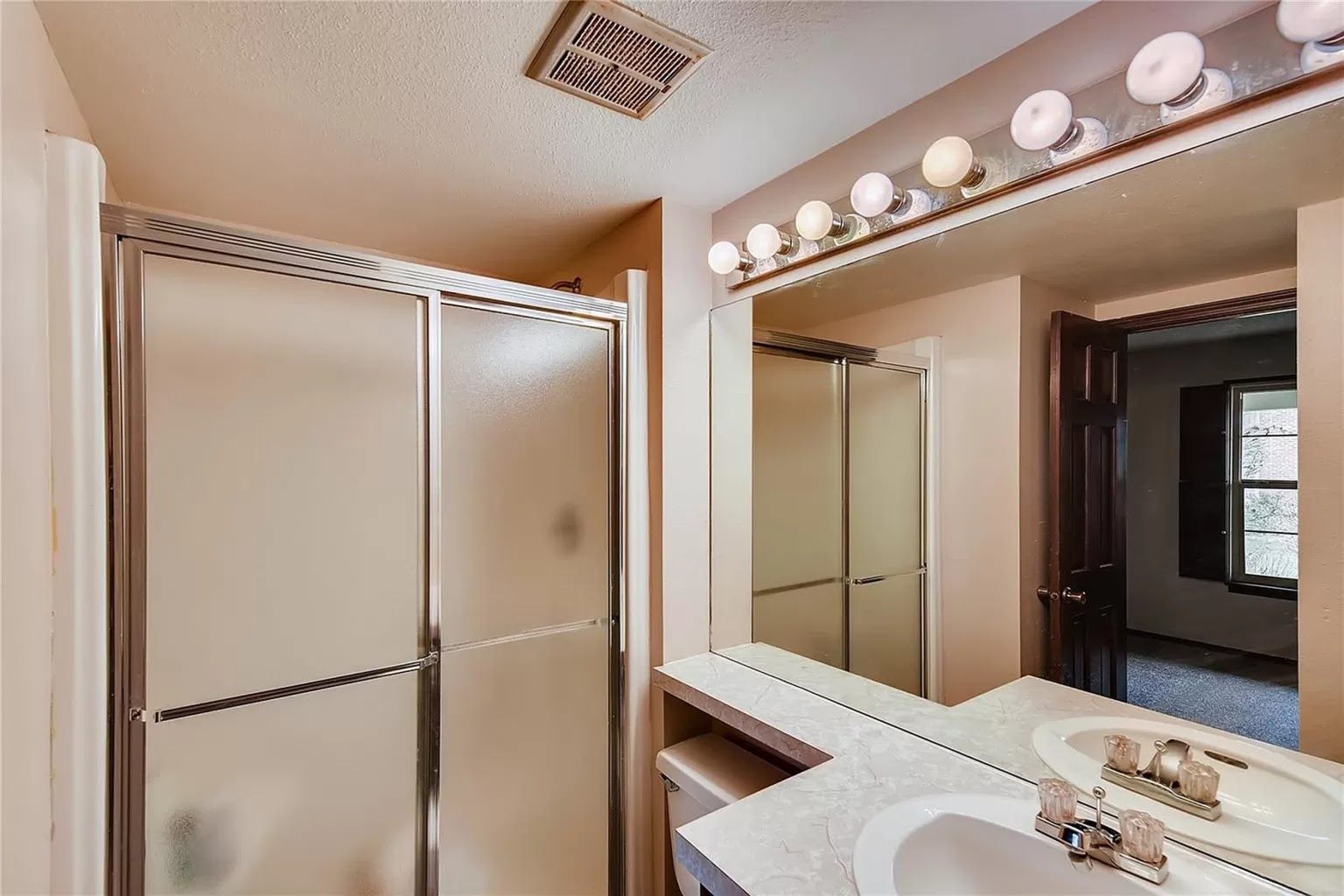 Main level bathroom before remodeling: frosted sliding shower doors, laminate vanity top and dated bulb light bar.