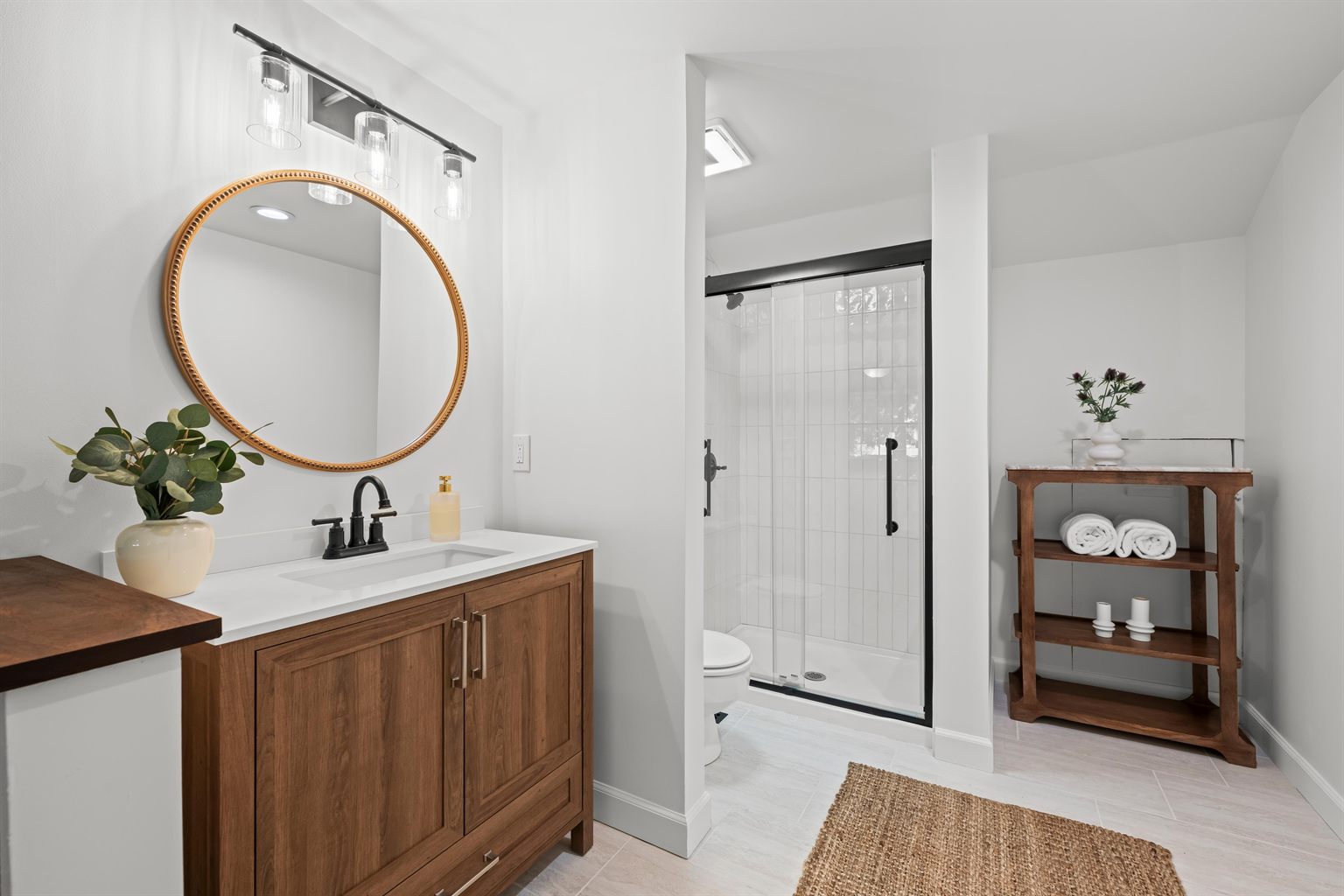 Primary bathroom after remodeling by SR Contractor LLC: walnut vanity with quartz countertop, round gold mirror, matte black fixtures and a tiled walk-in shower.