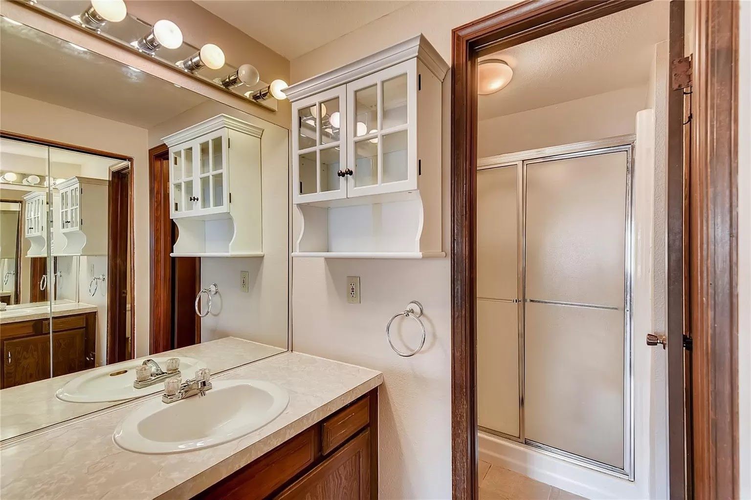 Primary bathroom before remodeling: oak vanity with laminate countertop, dated shower enclosure and beige walls.